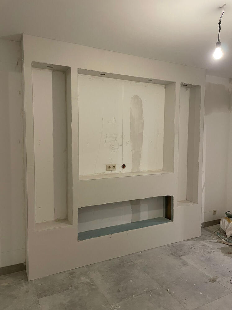 TV-wand met haardnis afgewerkt — S GYPFIX Ronse Geplamuurde gipsplaten TV-wand met nis voor elektrische haard en zijrekken voor decoratie - S GYPFIX Ronse